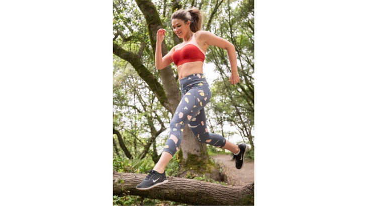 Woman in sports bra and leggings jumping over a log