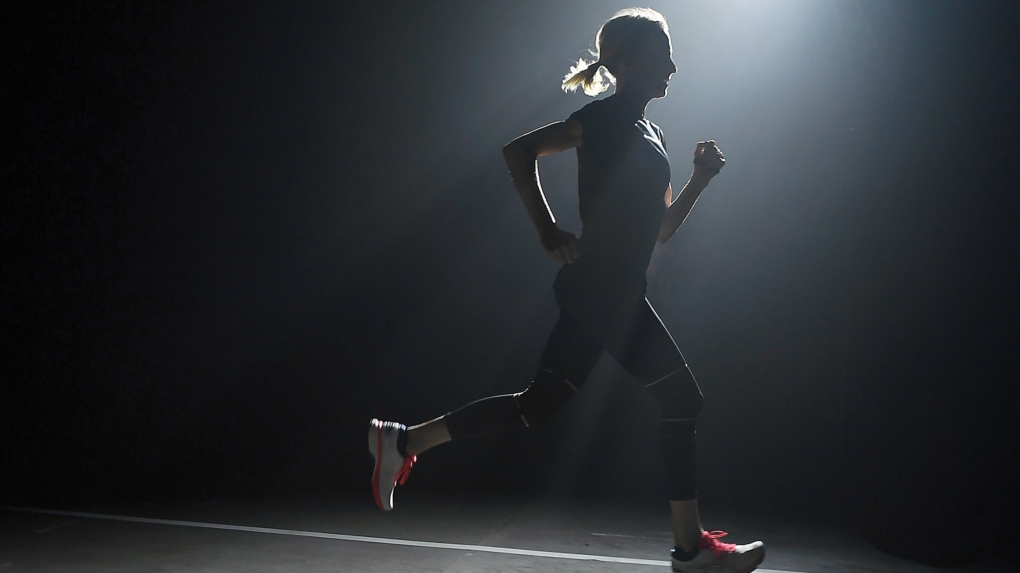 Deena Kastor running on a darkly lit indoor track