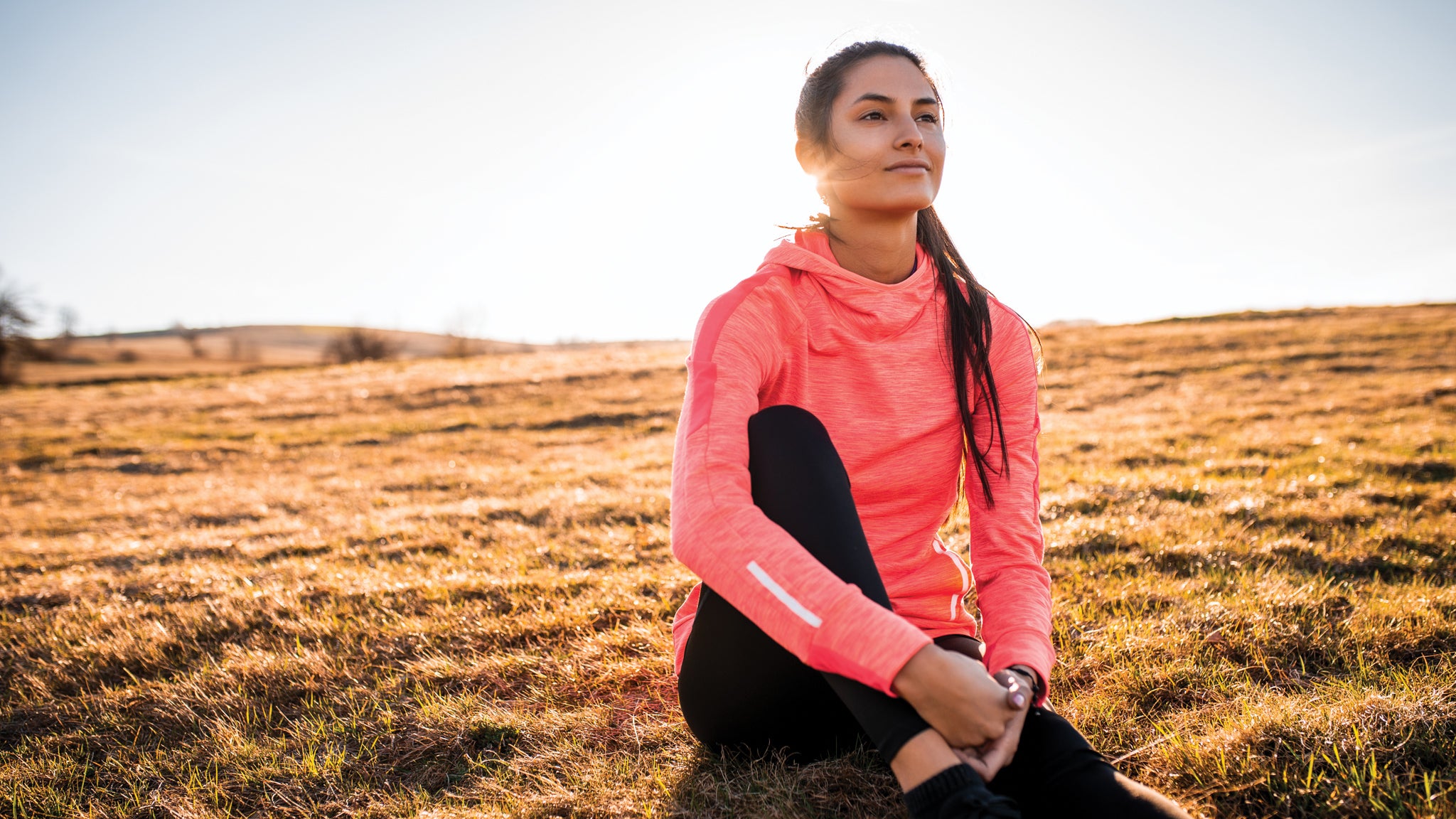 Athletic woman sits on a golden grassy hill in the sun