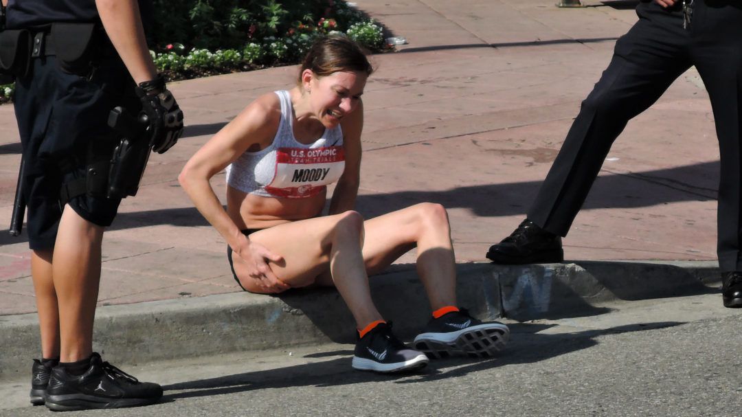 Tera Moody sits on a curb clutching her hamstring during the LA Marathon while experiencing a charley horse