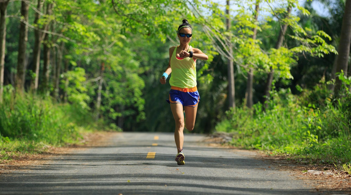 Young fitness woman running at morning lush forest trail.