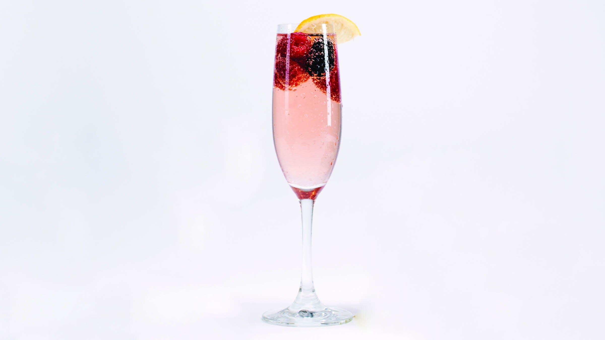 Sunshine spritz in a champagne glass with berries and lemon slice for garnish