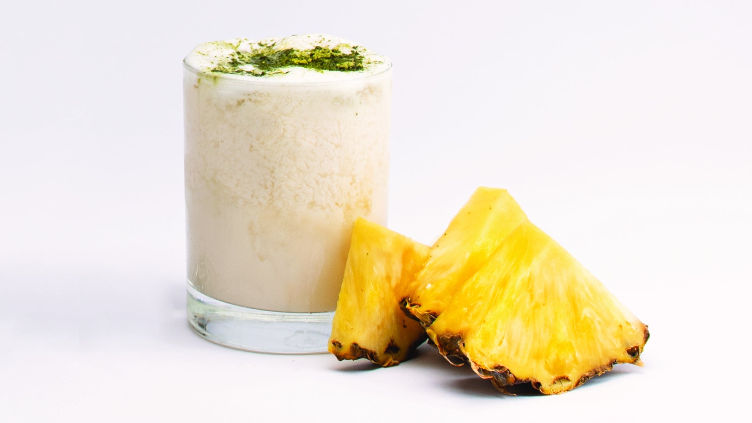 Tropical morning in a glass tumbler with matcha powder garnish, next to 3 pineapple slices