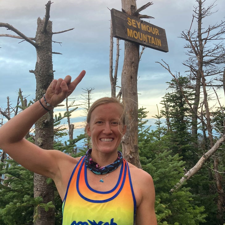 A woman stands in front of a sign for Seymour Mountain and points at it