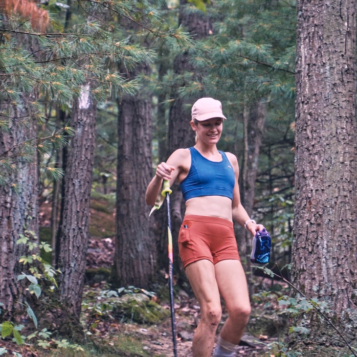 A woman jogs through a forest with a hiking pole