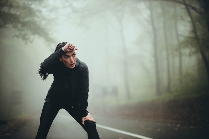 Exhausted female athlete taking a break after exercising in foggy forest.