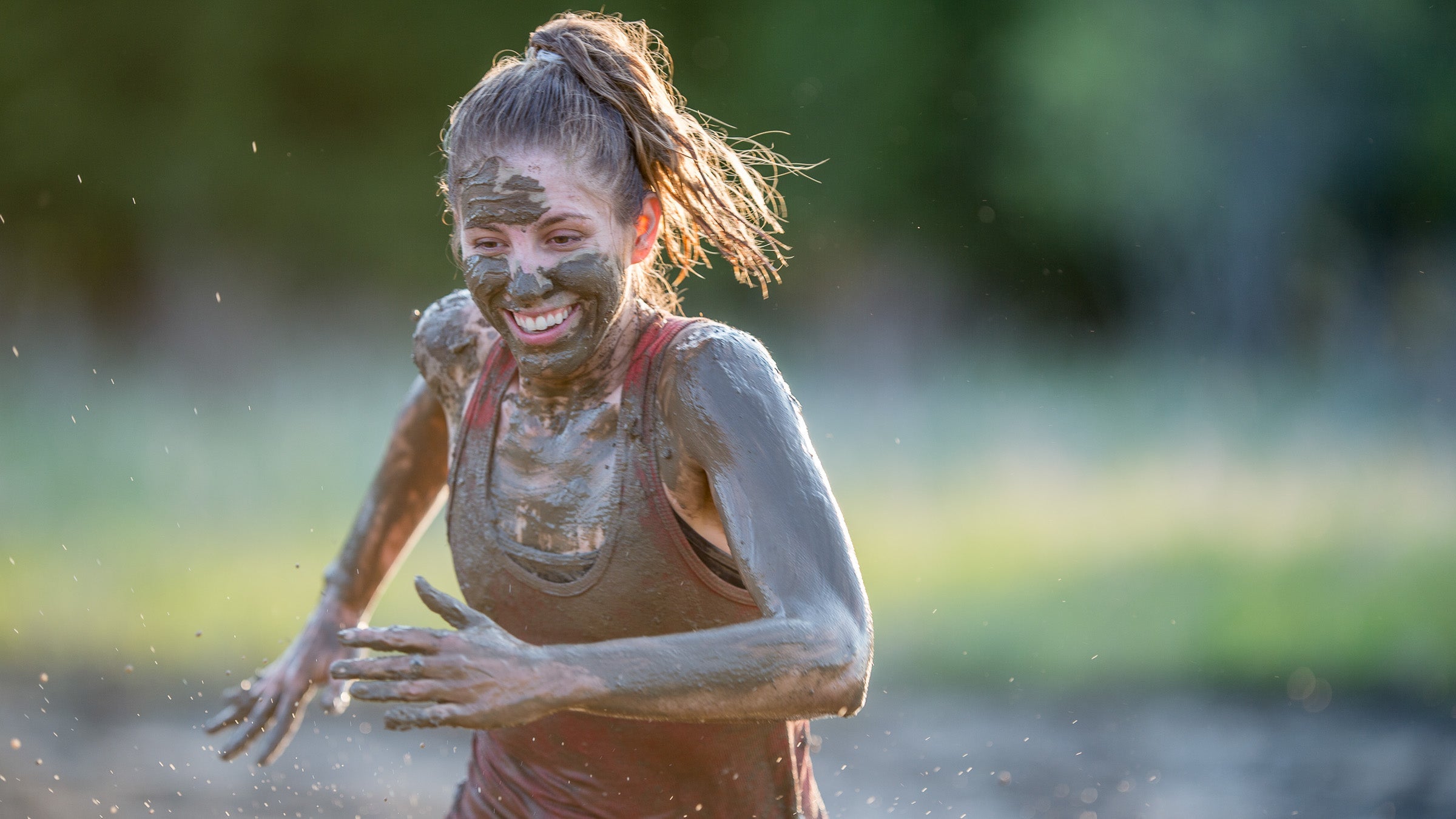 Smiling woman running while covered in mud