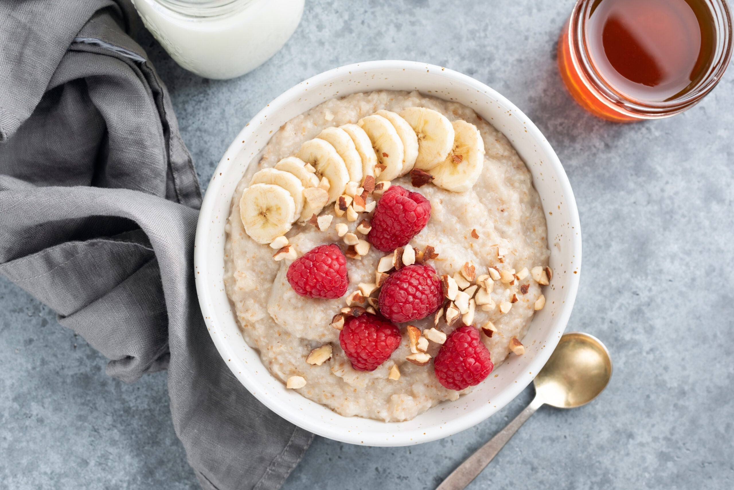 Oatmeal porridge with raspberries and banana in bowl on concrete background, table top view. Healthy breakfast food, dieting and clean eating concept