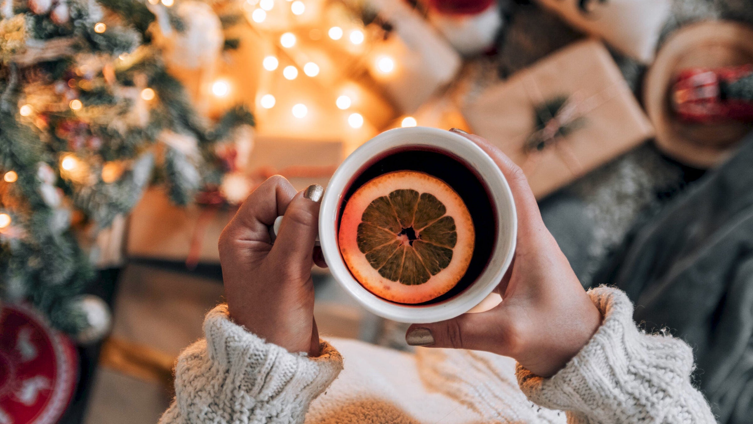 Orange slice in mug of tea over Christmas decorations