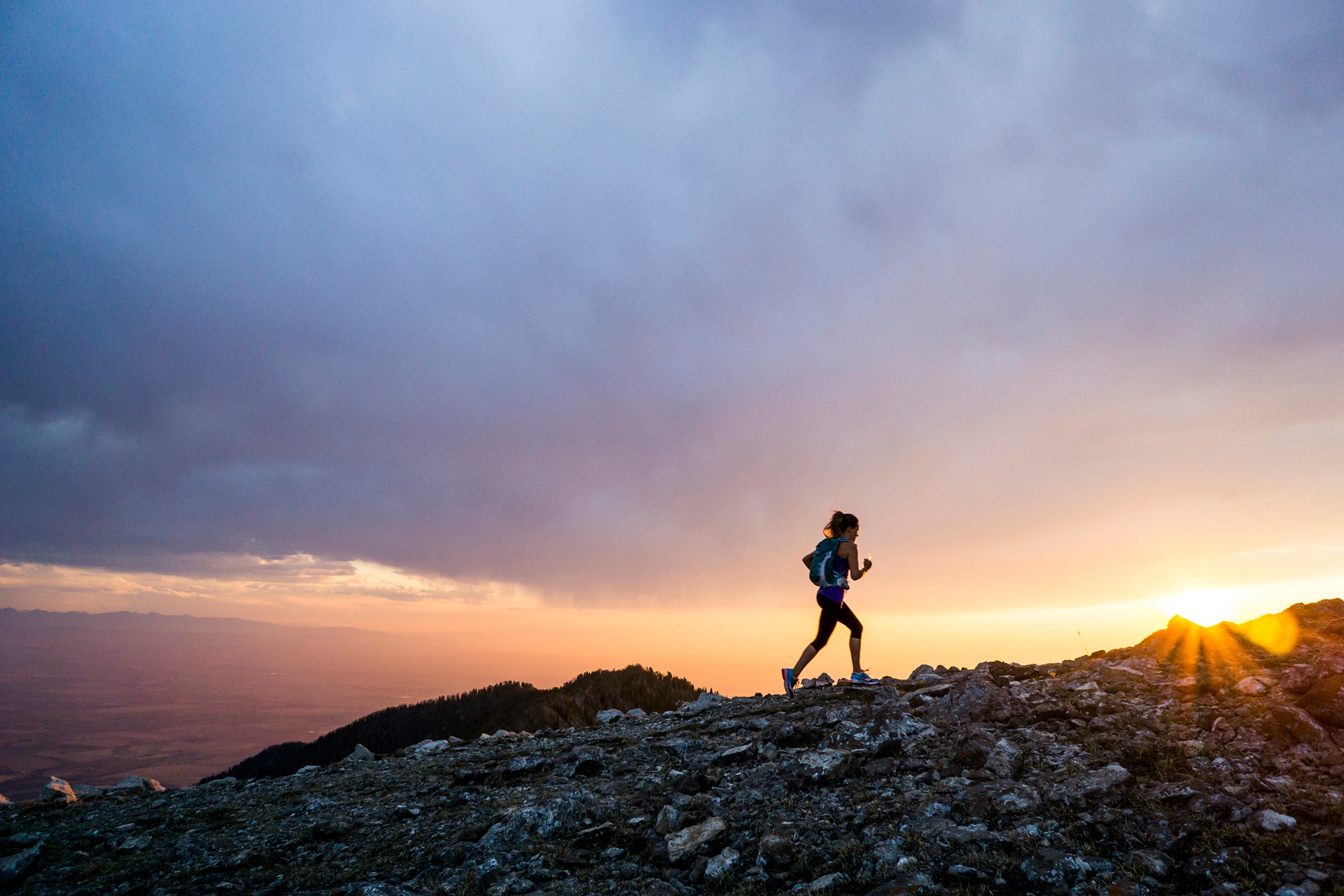 A woman trail running at as sunset along a mountain pass.