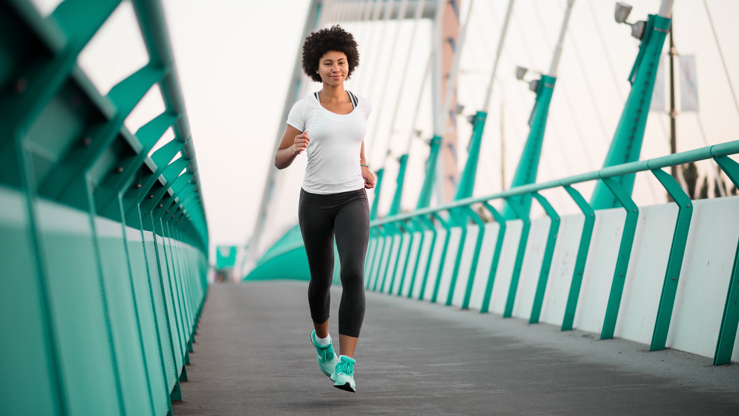 Woman in teal shoes jogging across a teal bridge