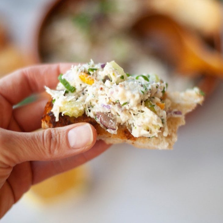 a white woman's hand holding a piece of toast with chicken salad on top