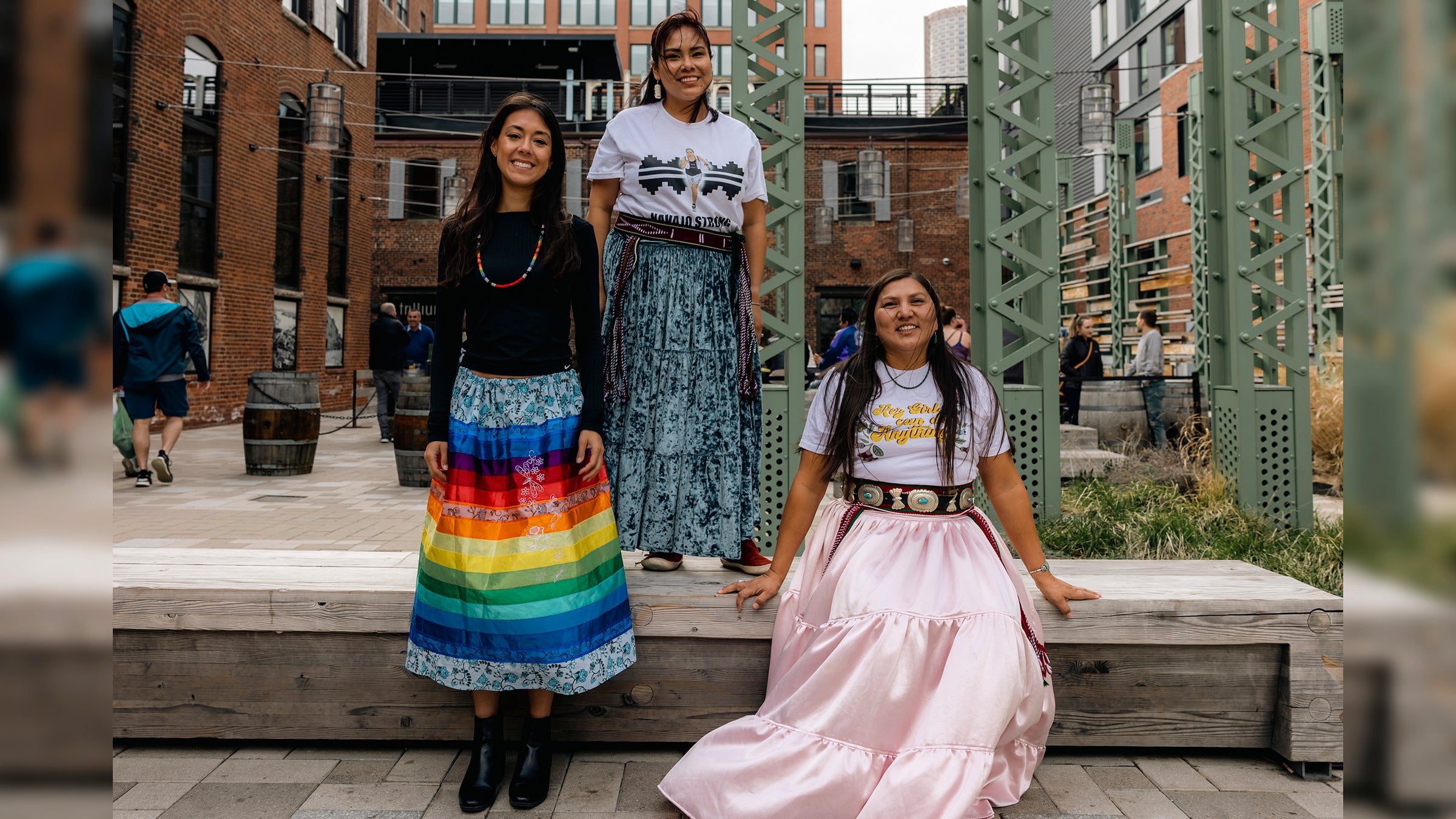 Three Indigenous woman pose in traditional garb in an urban Boston setting