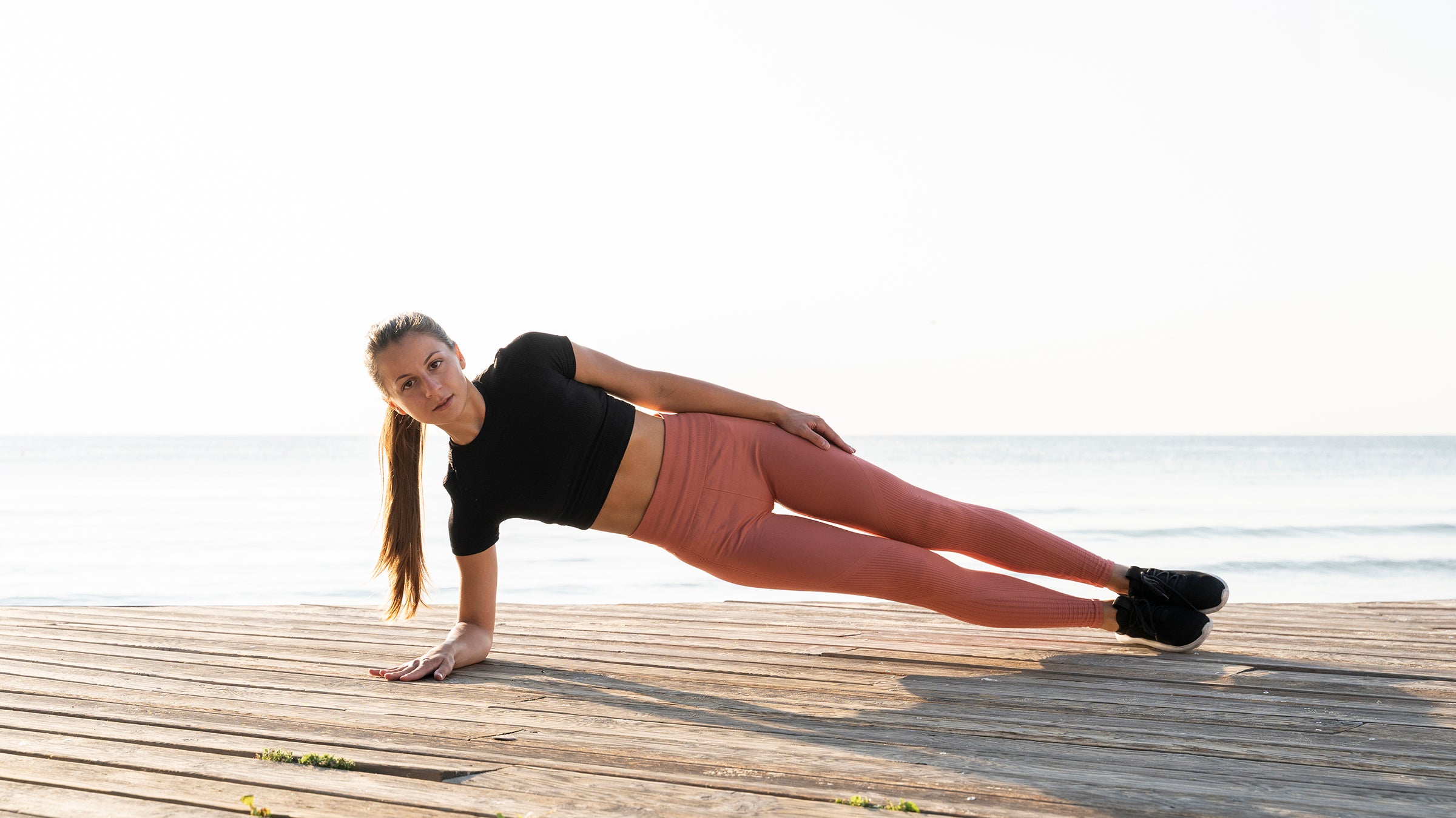 woman performing side plank, a cross-training exercise for runners, on a boardwalk
