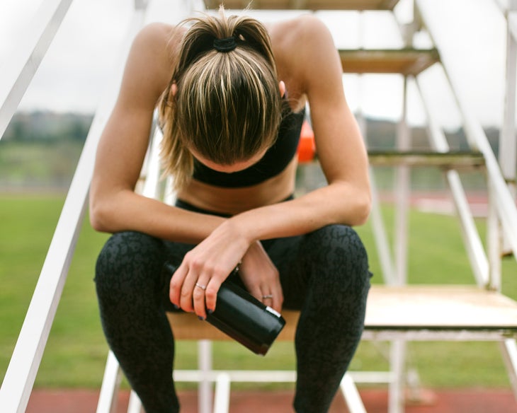 female athlete hanging her head sitting on steps exhausted during a track workout