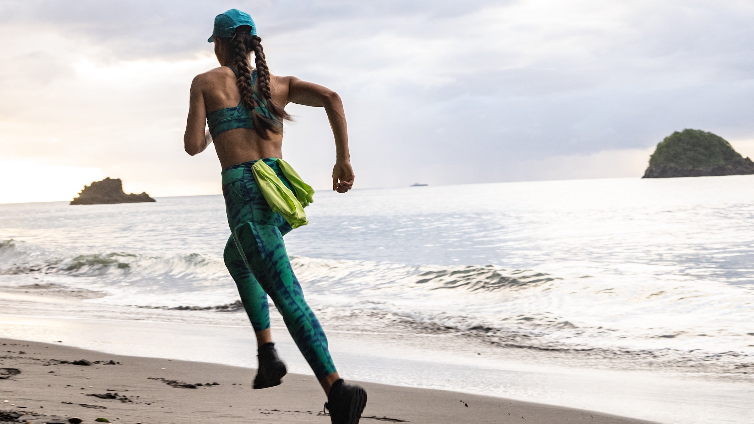 A woman runs on a beach in colorful green activewear
