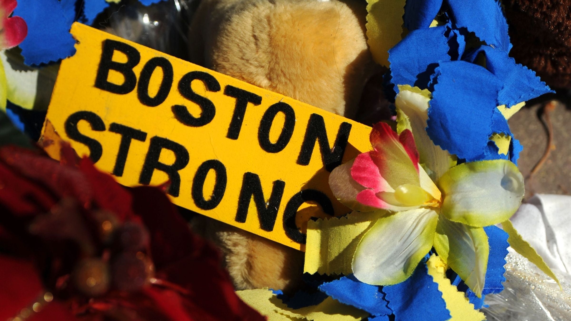 A yellow sign that says Boston Strong surrounded by yellow and blue flowers