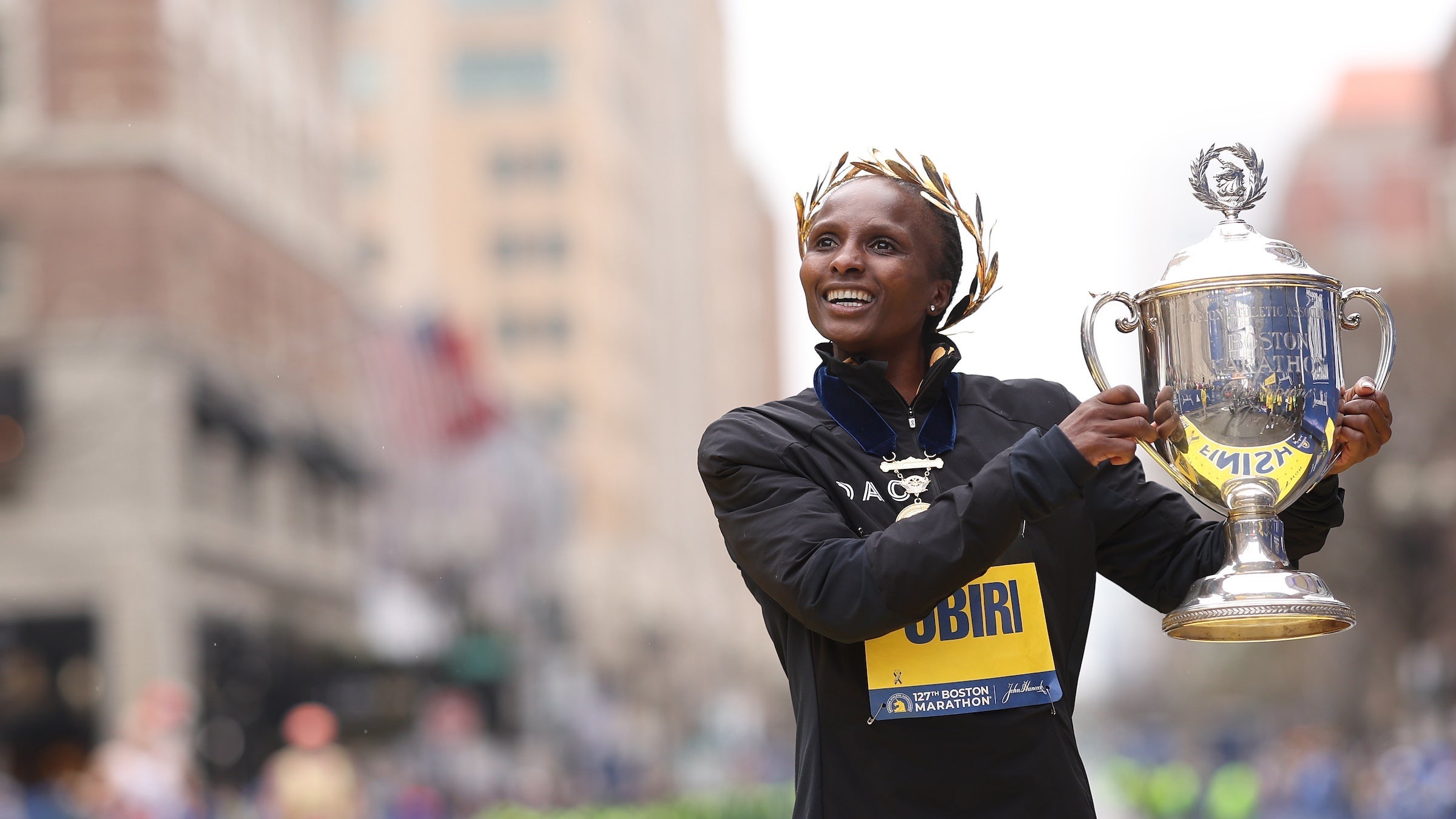 Obiri holds up a trophy with laurels on her head at the finish line of the boston marathon