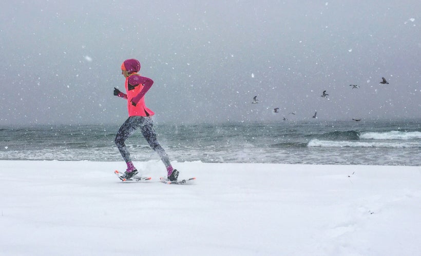 Woman running along winter shore in snowshoes