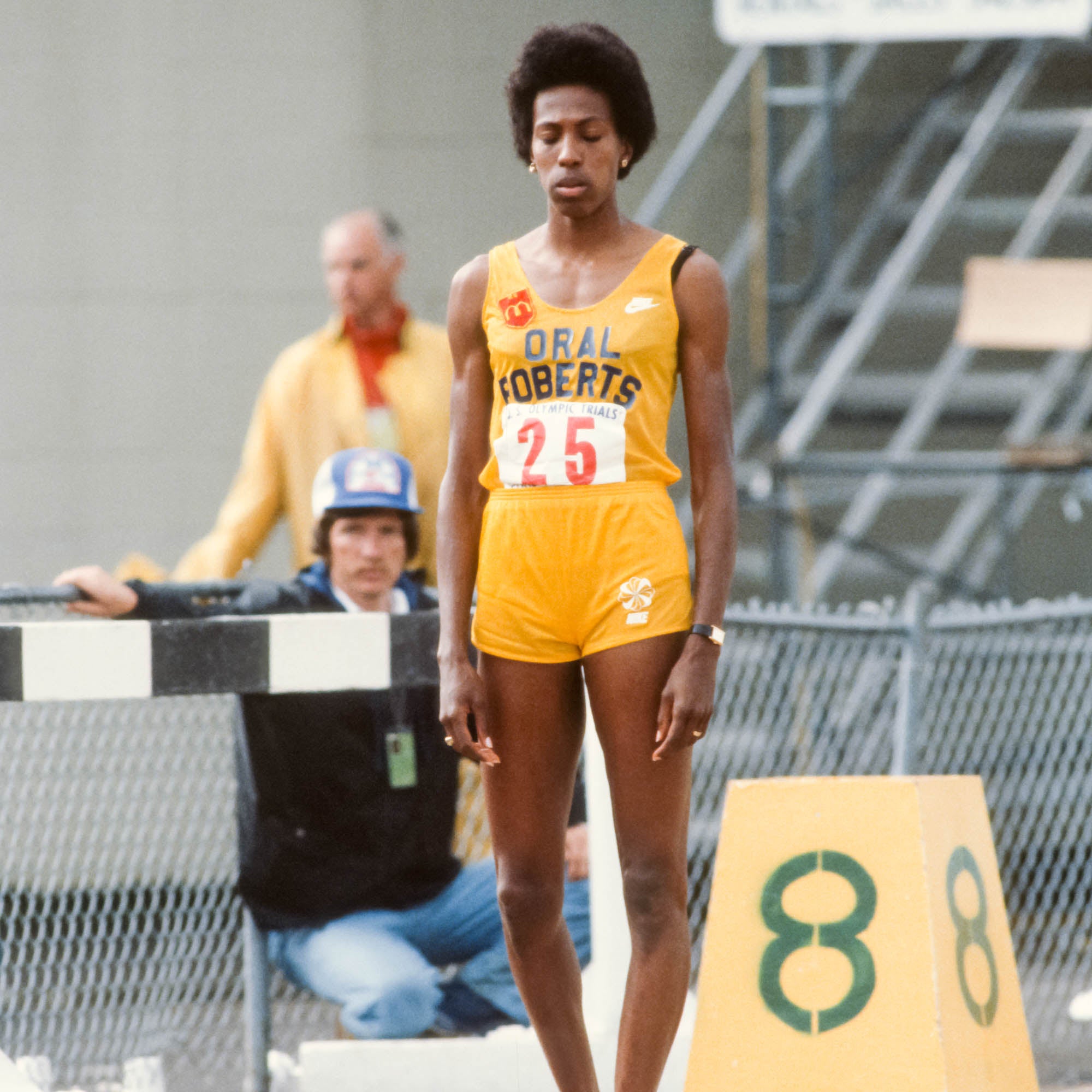 A tall woman in yellow stands alone on a wet track