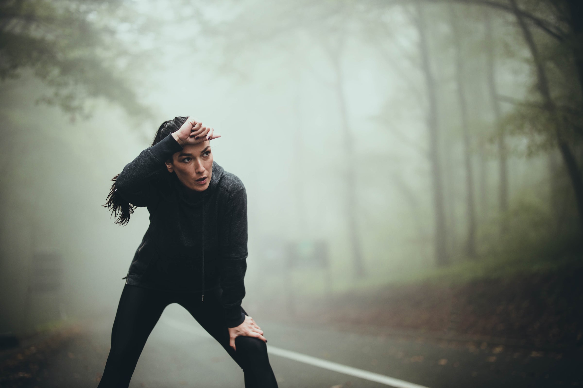 Exhausted female athlete taking a break after exercising in foggy forest.